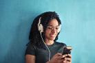A woman scrolling on her phone, listening to something on her headphones. Credit: Canva
